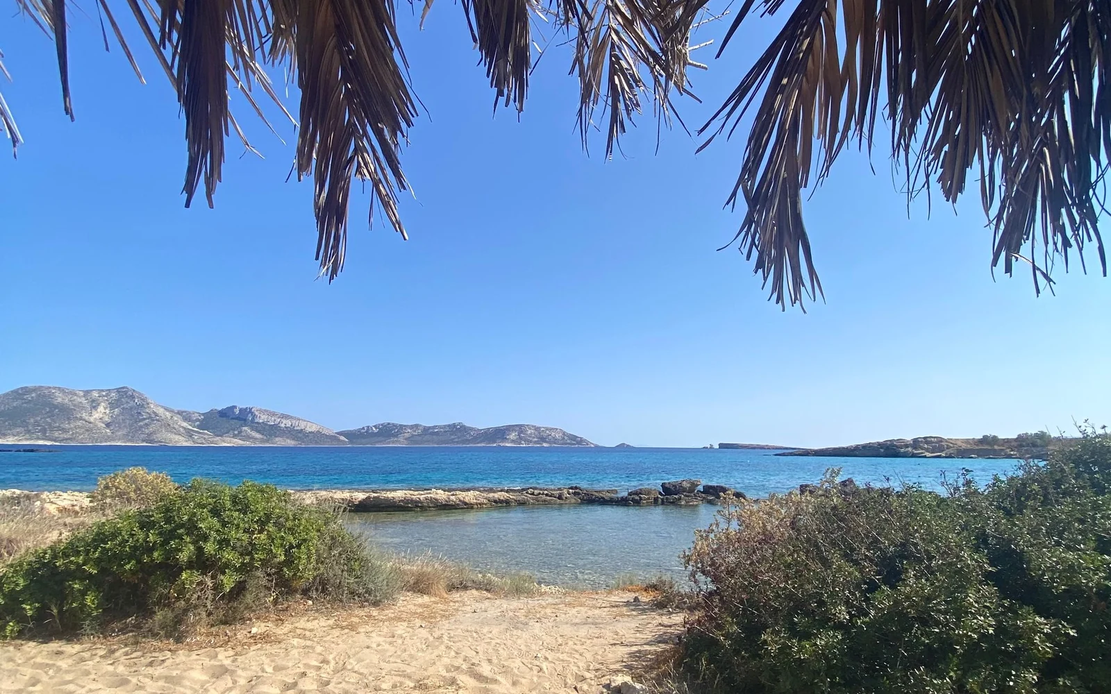 A sandy beach and blue sea on Naxos, viewed from beneath a shade canopy.