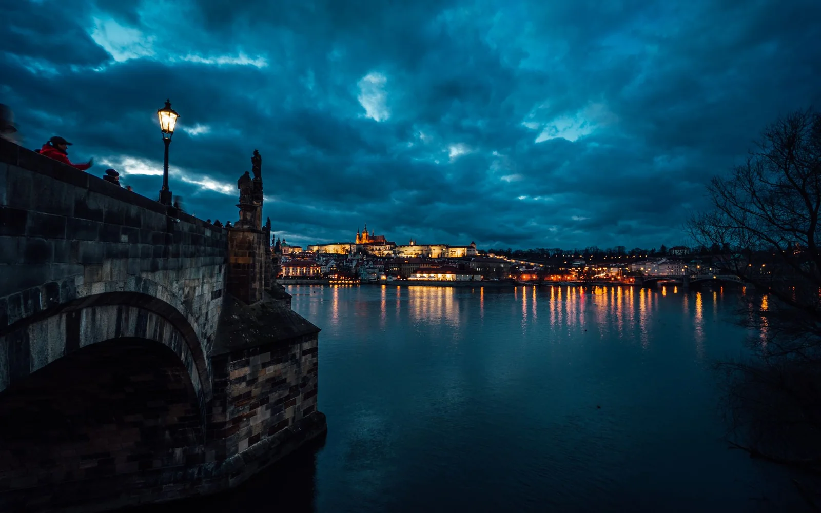 Charles Bridge and Prague's illuminated skyline reflected in the Vltava at dusk.