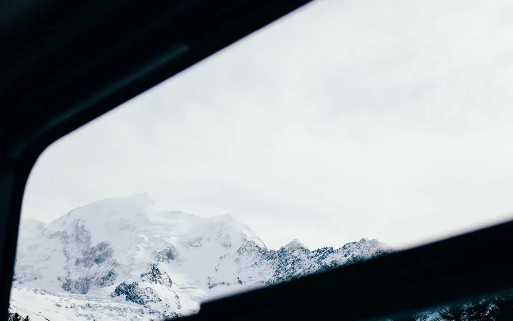 Snow-covered mountains seen through the dark frame of a train window; illustrative winter rail photograph, not identified as the Gotthard line.